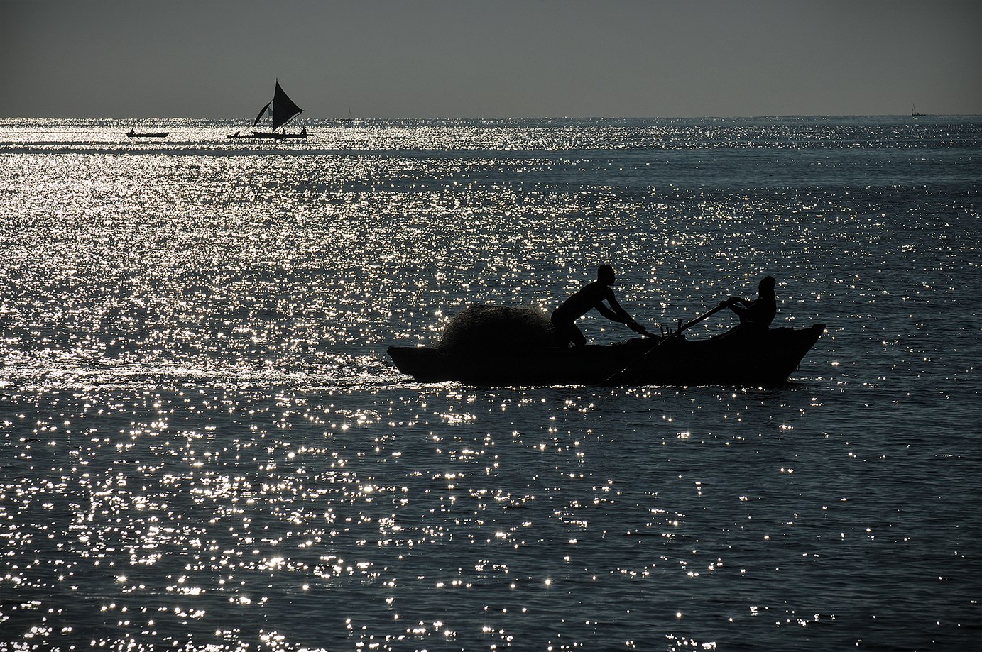 Silhouette d’une barque sur une mer scintillante.