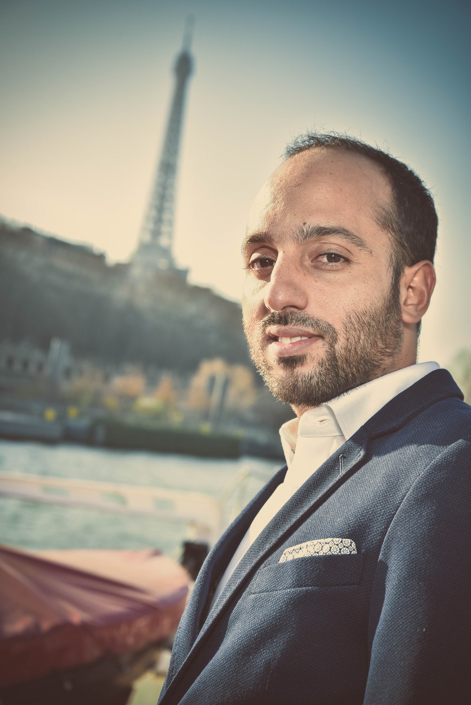 Portrait d’un homme en costume devant la Seine et la tour Eiffel.