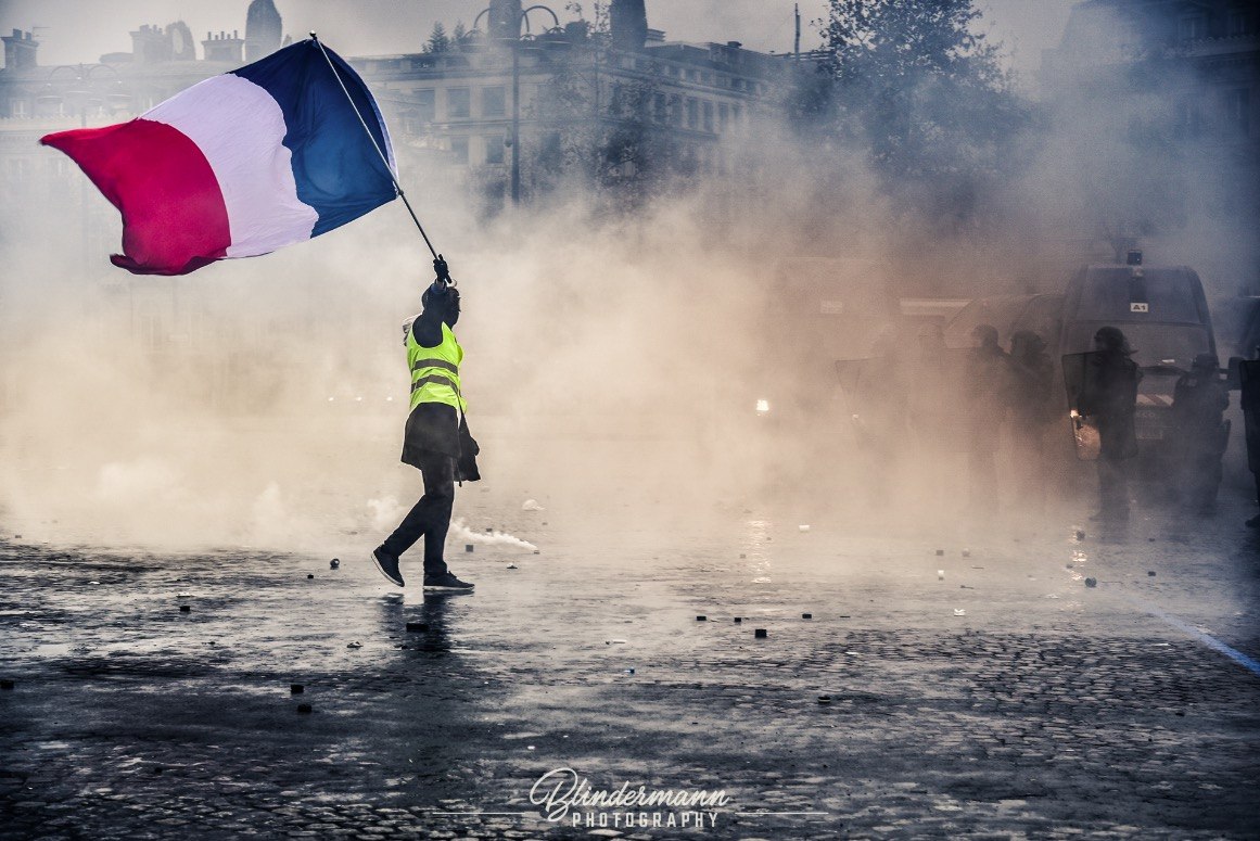 Une personne portant un drapeau français dans une rue enfumée.